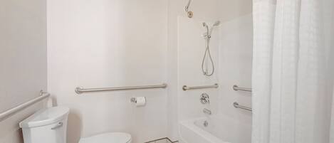 A bathroom with a toilet, a shower, and a bathtub, equipped with grab bars and a towel rack.