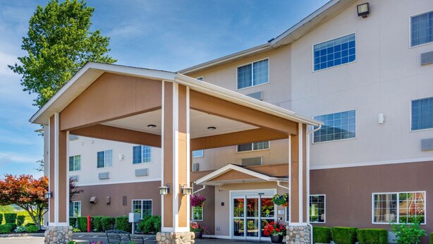 A multi-story hotel with a covered entrance, stone pillars, and a parking lot.