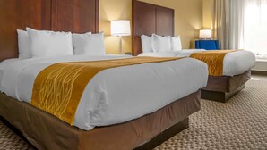 A hotel room with two beds, a wooden headboard, a beige carpet, and a window with curtains.