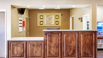 Un espace d’accueil comprenant un comptoir de réception en bois, un téléviseur fixé au mur et un luminaire fixé au mur.