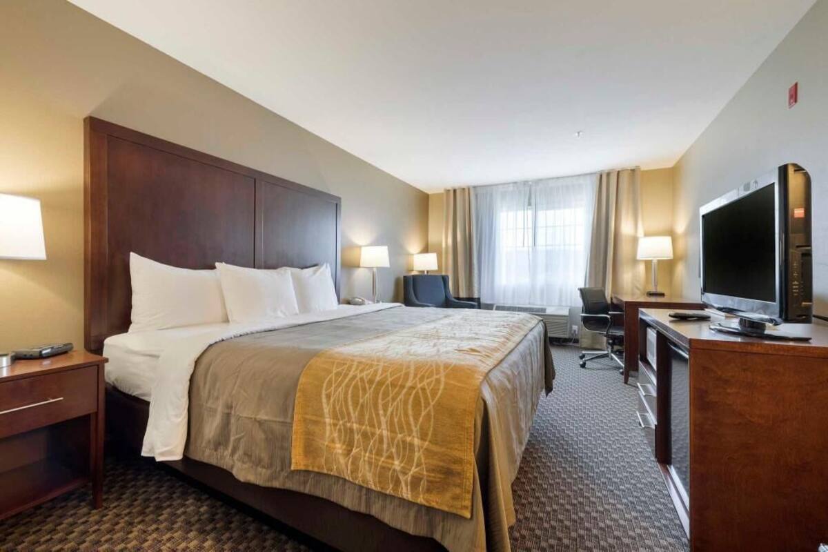 A hotel room with a large bed, bedside lamps, a desk with a television, and a chair.
