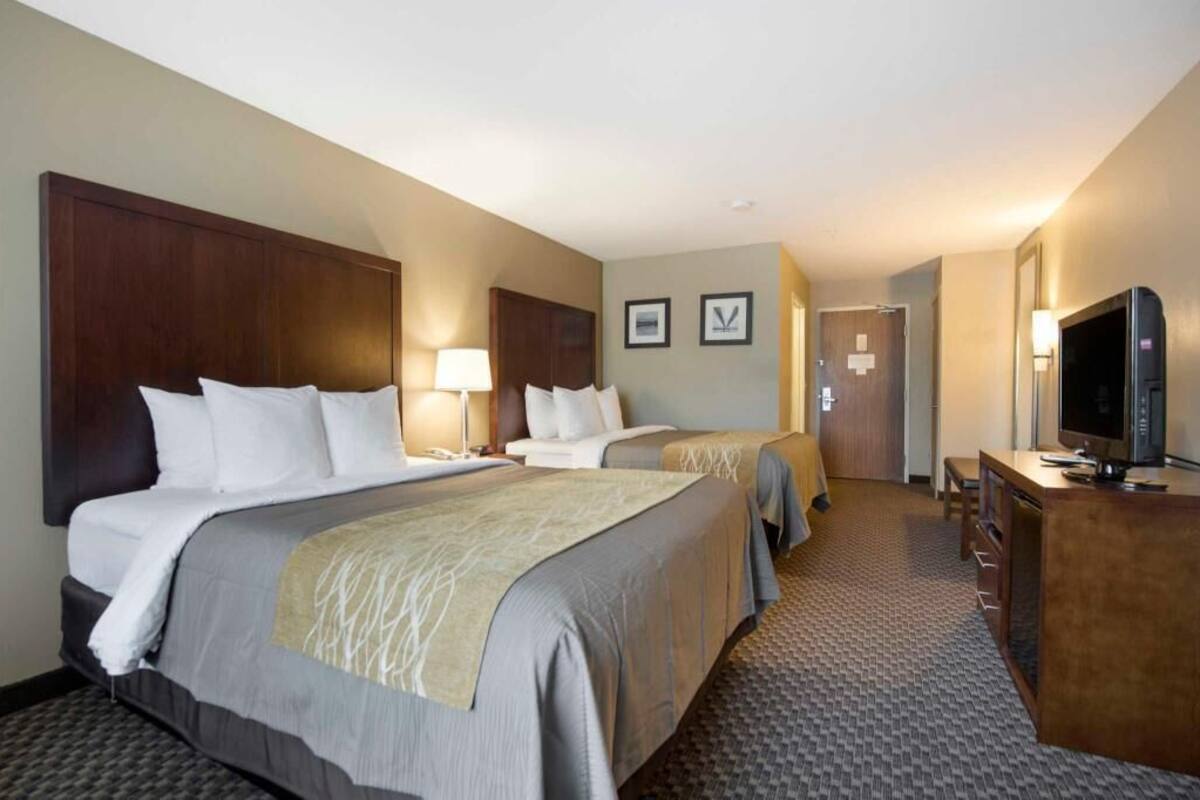 A hotel room with two beds, a desk with a television, and a door leading to another room.