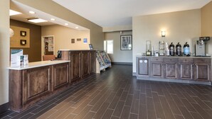 A reception area with a wooden reception desk, a bulletin board, and a coffee station with various appliances.