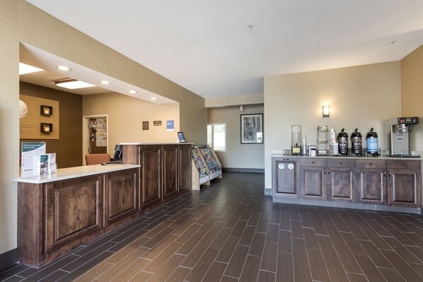 A reception area with a wooden reception desk, a bulletin board, and a coffee station with various appliances.