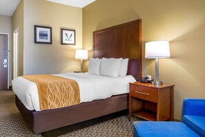 A hotel room with a large bed, two bedside lamps, a wooden nightstand, a blue chair, and two framed pictures on the wall. - Comfort Inn Auburn - Seattle (Auburn)