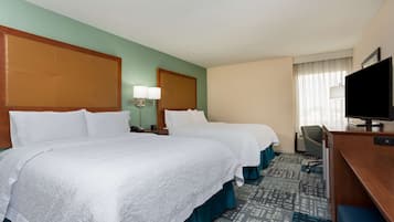 A hotel room with two beds, a desk with a television, a chair, and a lamp.