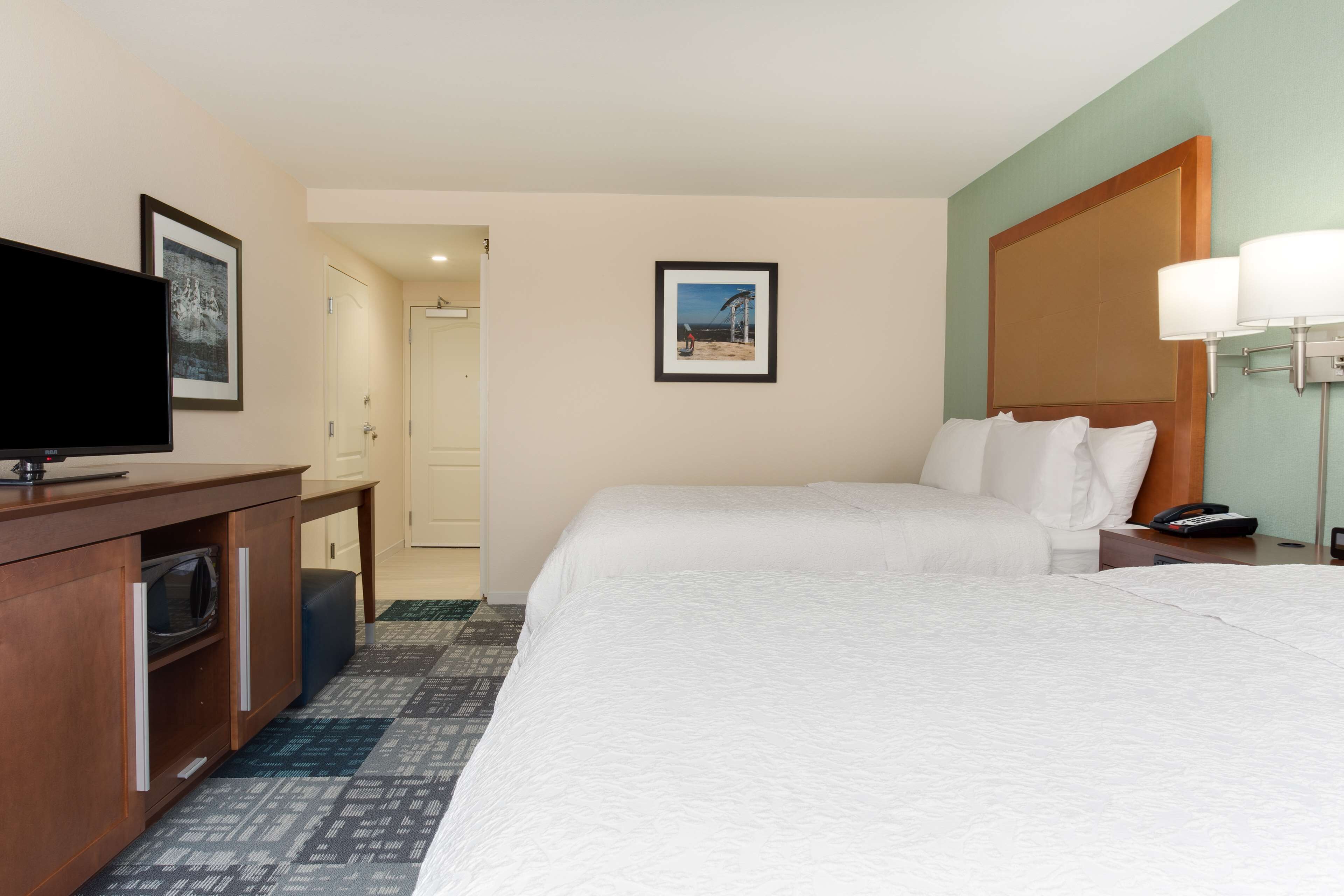 Habitación de hotel con cama, escritorio con televisor, microondas y un cuadro en la pared.