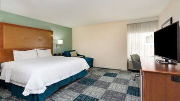A hotel room with a large bed, a desk with a TV, a chair, and a window with curtains.