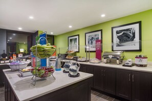 A modern kitchen with a buffet setup, including a fruit bowl, coffee makers, and a food display.