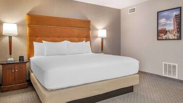 A hotel room with a large bed, two bedside tables, a nightstand, a wall-mounted picture, and a vent.