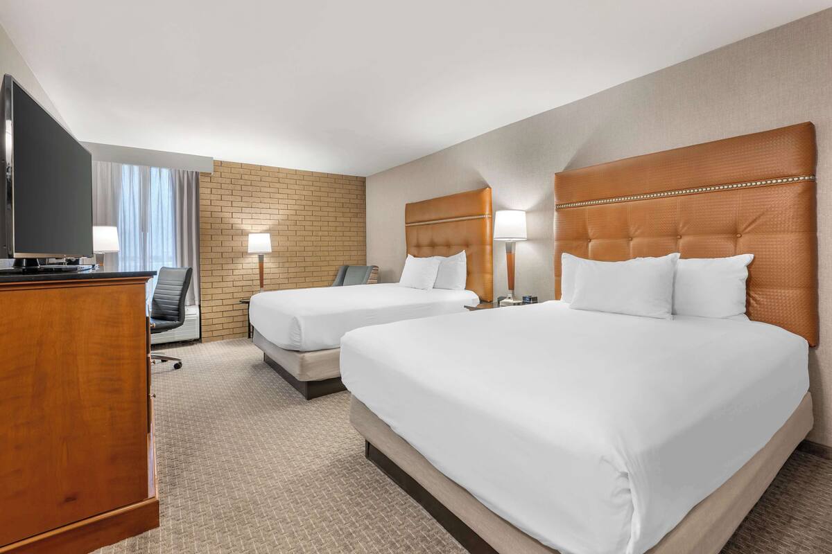 A hotel room with two beds, a TV, a desk, and a chair.