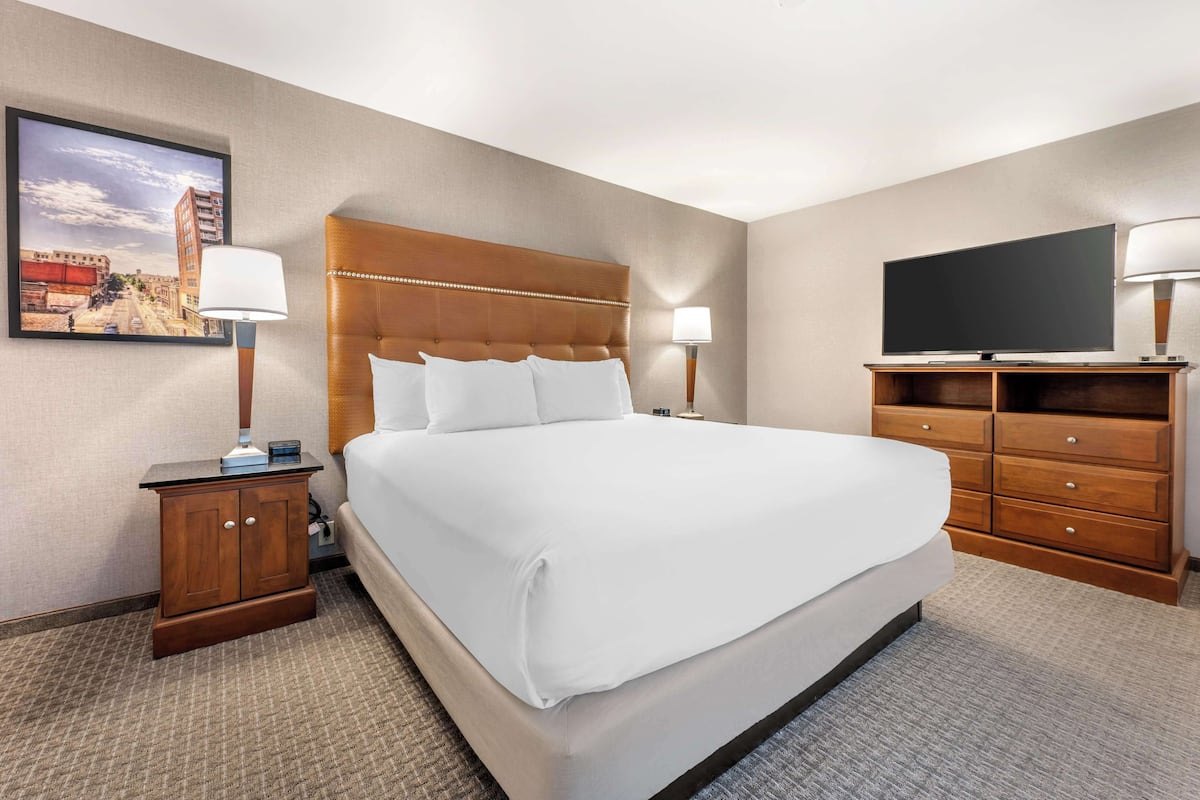 A hotel room with a large bed, wooden nightstands, a flat-screen TV, and a framed cityscape picture on the wall.
