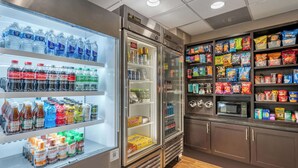 A self-service beverage and snack station with refrigerated drinks, microwaves, and a variety of snacks. - Drury Inn & Suites Champaign (Champaign)
