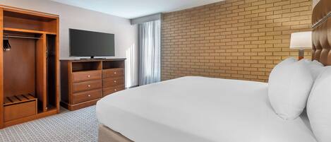 A hotel room with a large bed, a TV on a stand, a wardrobe, and a brick accent wall.