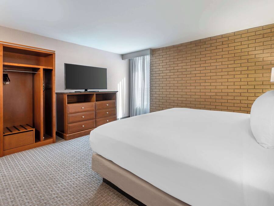 Habitación de hotel con una cama grande, un televisor sobre un soporte, un armario y una pared decorativa de ladrillo.