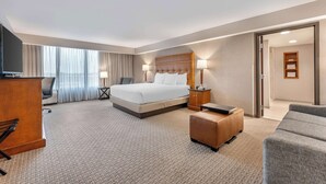 A hotel room with a large bed, a desk with a computer, a TV, and a seating area with a sofa and armchair. - Drury Inn & Suites Champaign (Champaign)