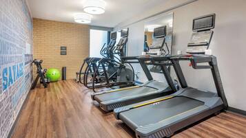 Un gimnasio con cintas de correr, pelotas de ejercicio y un espejo.