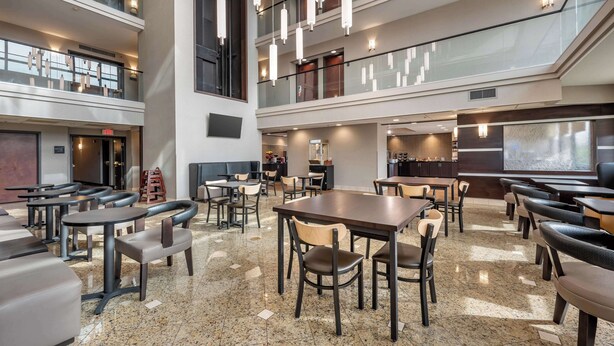 A spacious indoor area with multiple seating arrangements, including tables and chairs, and a high ceiling with hanging lights. - Drury Inn & Suites Champaign (Champaign)