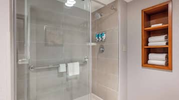 A modern bathroom with a glass-enclosed shower, a wooden towel rack, and a shelf with toiletries.