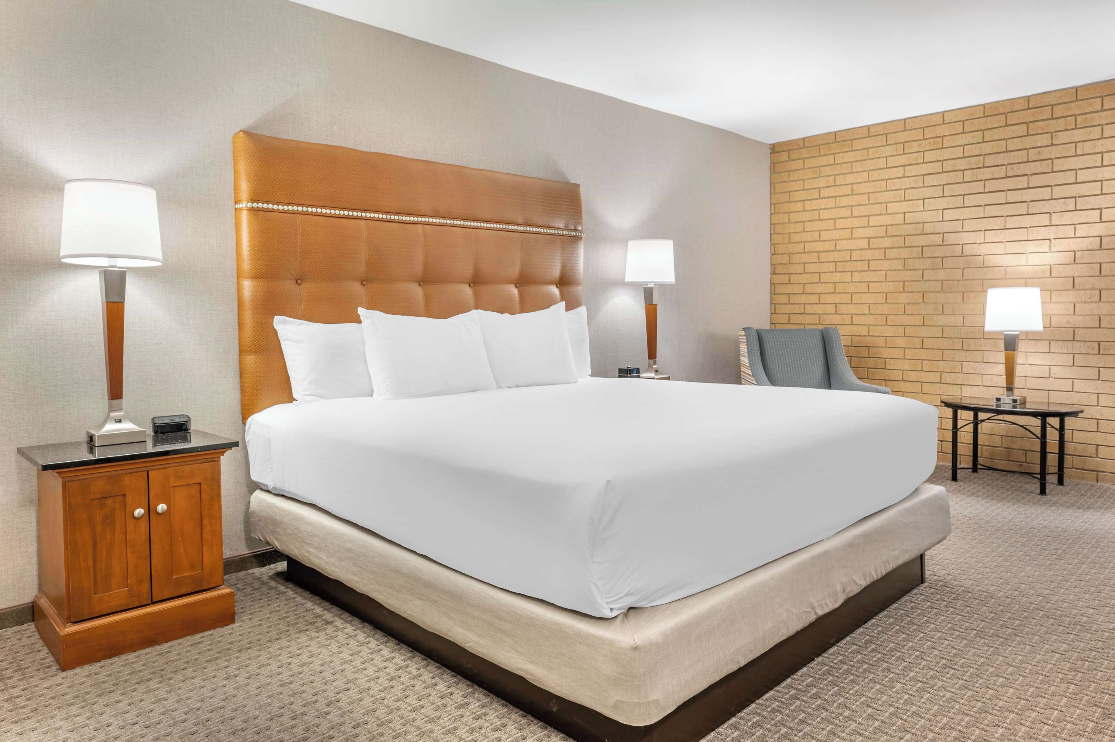 A hotel room with a large bed, two bedside tables with lamps, a wooden headboard, and a brick-patterned wall.