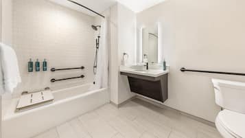 A modern bathroom with a white bathtub, a sink, and a toilet. There are grab bars next to the bathtub and toilet, and a showerhead above the bathtub.