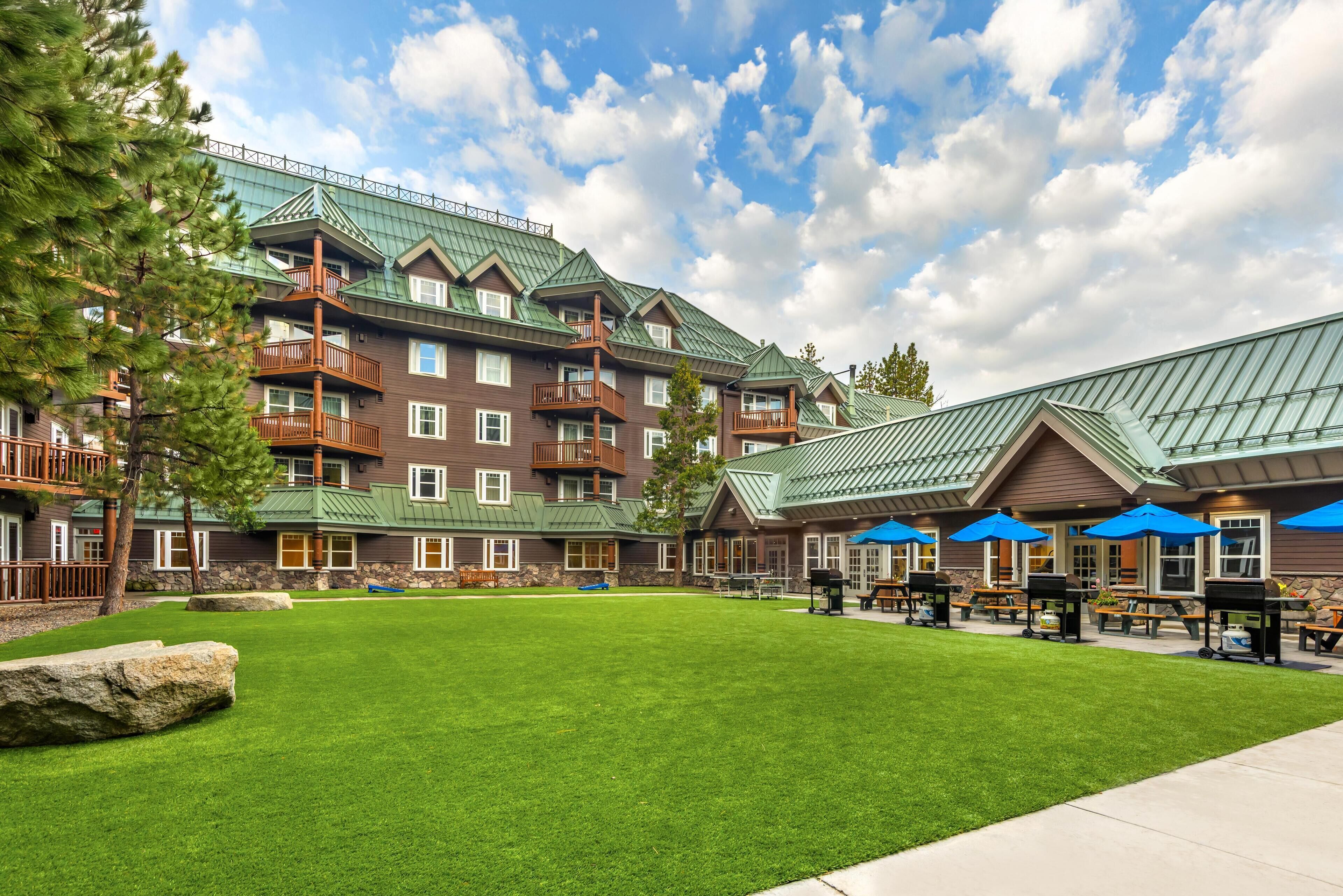 A multi-story hotel with a green roof, outdoor seating area, and a well-maintained lawn.