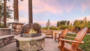 An outdoor seating area with a stone fire pit, wooden chairs, and a view of the surrounding forest. - Hilton Vacation Club Lake Tahoe Resort South (South Lake Tahoe)