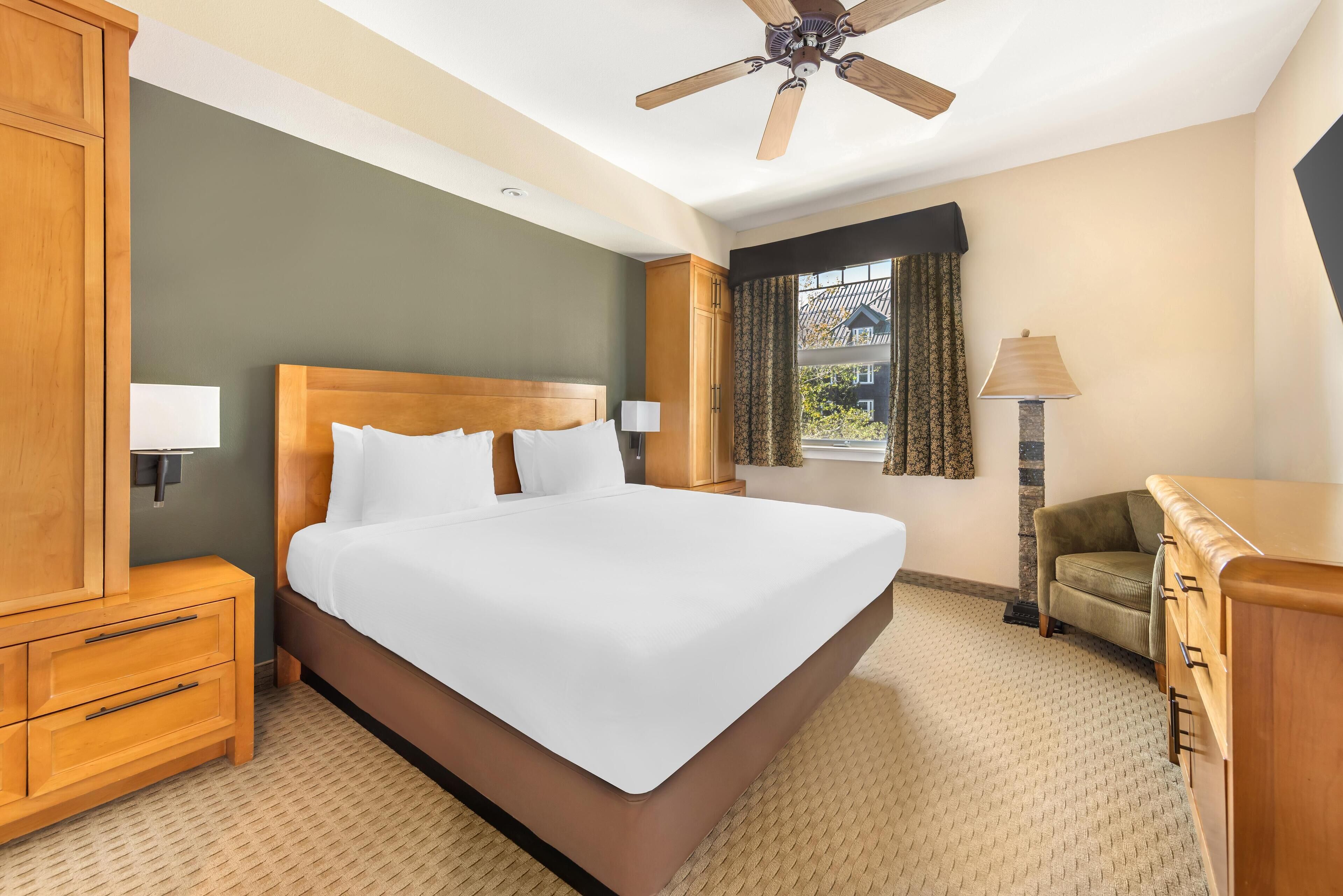 A hotel room with a large bed, wooden nightstands, a desk, and a ceiling fan.