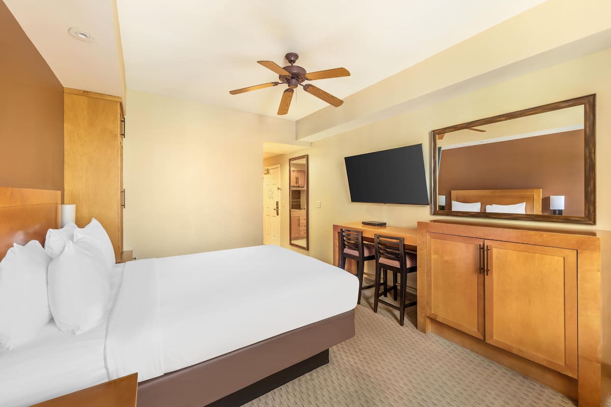 A hotel room with a large bed, wooden headboard, a desk with two chairs, a television, and a wardrobe.