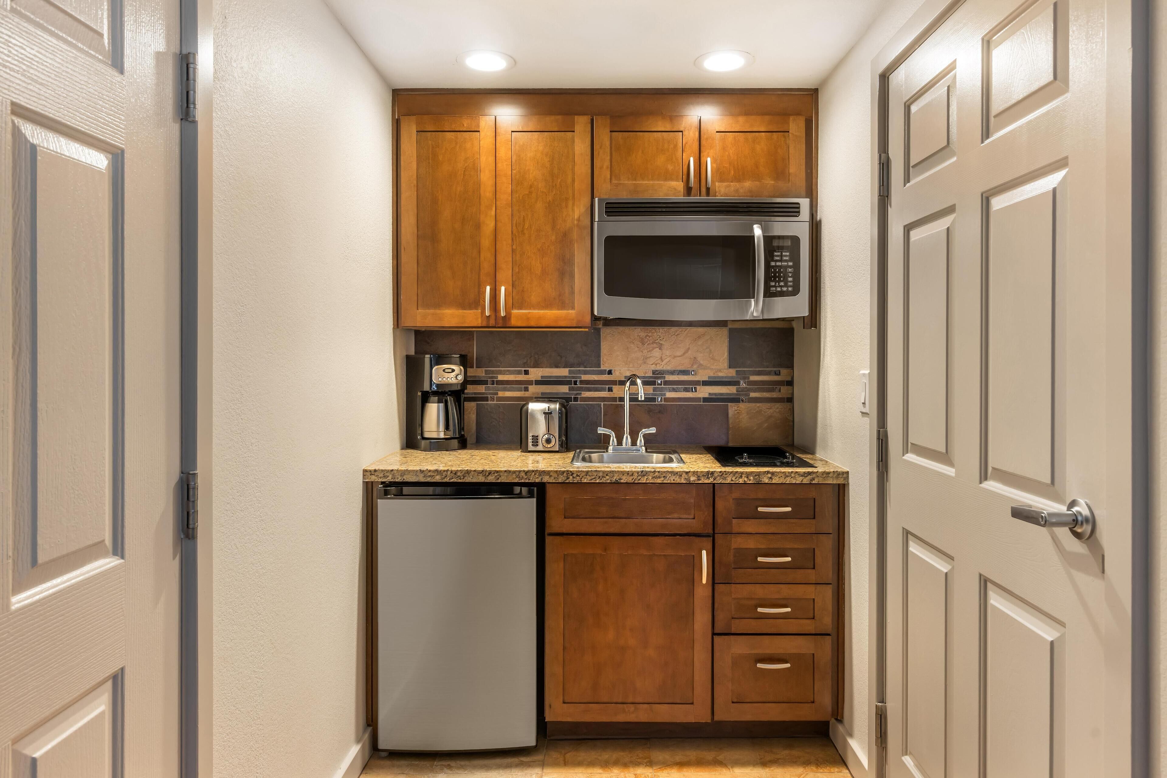 A compact kitchen with wooden cabinets, a stainless steel microwave, a dishwasher, and a granite countertop.
