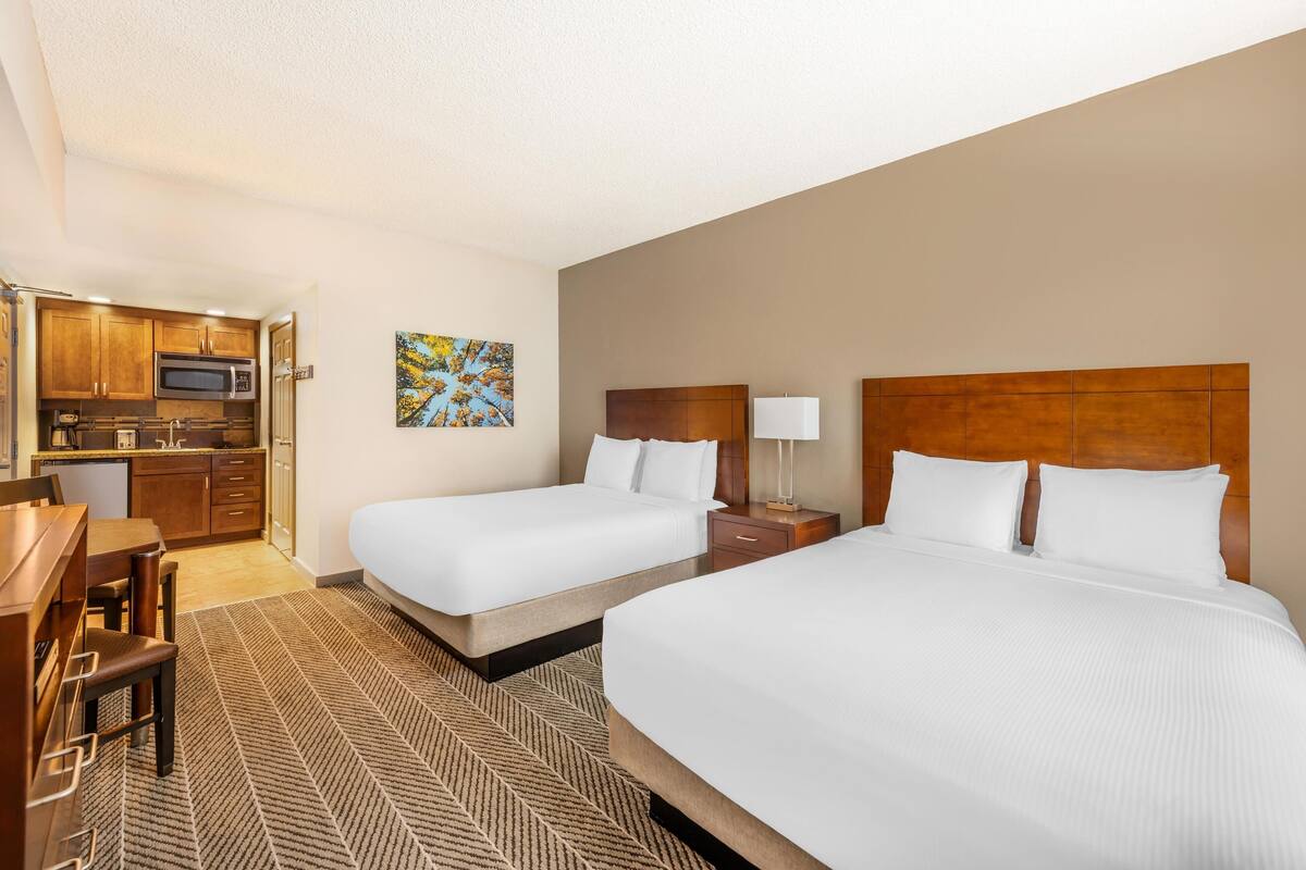 A hotel room with two beds, a desk, a microwave, and a small kitchenette.