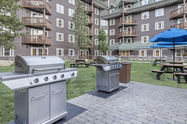 A patio area with a grill and picnic tables, surrounded by a multi-story building with balconies.