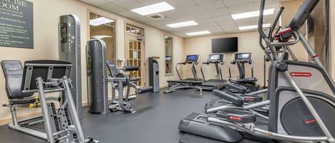 Un gimnasio con diversos equipos de ejercicio, incluyendo cintas de correr, elípticas y máquinas de pesas.