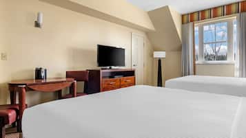 A hotel room with two beds, a desk with a flat-screen TV, a coffee maker, and a lamp.