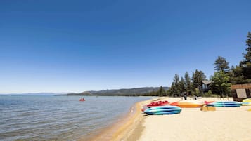 A beach with kayaks lined up on the sand, a clear sky, and a calm lake in the background.