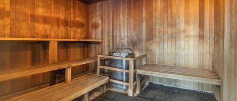 A sauna with wooden benches and a metal container.