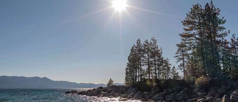 Un ciel dégagé, avec un soleil brillant qui illumine une côte rocheuse bordée d’arbres.