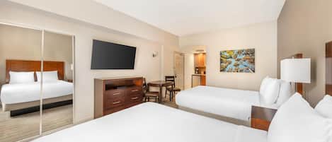 A hotel room with two beds, a desk, a chair, a TV, and artwork on the wall.