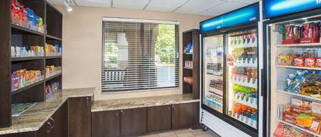 Un distributeur automatique de collations et de boissons en libre-service, doté de compartiments réfrigérés, d’une fenêtre avec des stores et d’un sol carrelé.