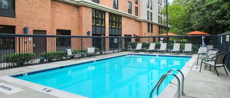 A swimming pool with lounge chairs and a brick building in the background.