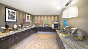 Una cocina moderna con un espacio tipo bufé, que incluye una máquina para gofres, una estación de café y varios recipientes con alimentos.