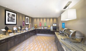 Una cocina moderna con un espacio tipo bufé, que incluye una máquina para gofres, una estación de café y varios recipientes con alimentos.