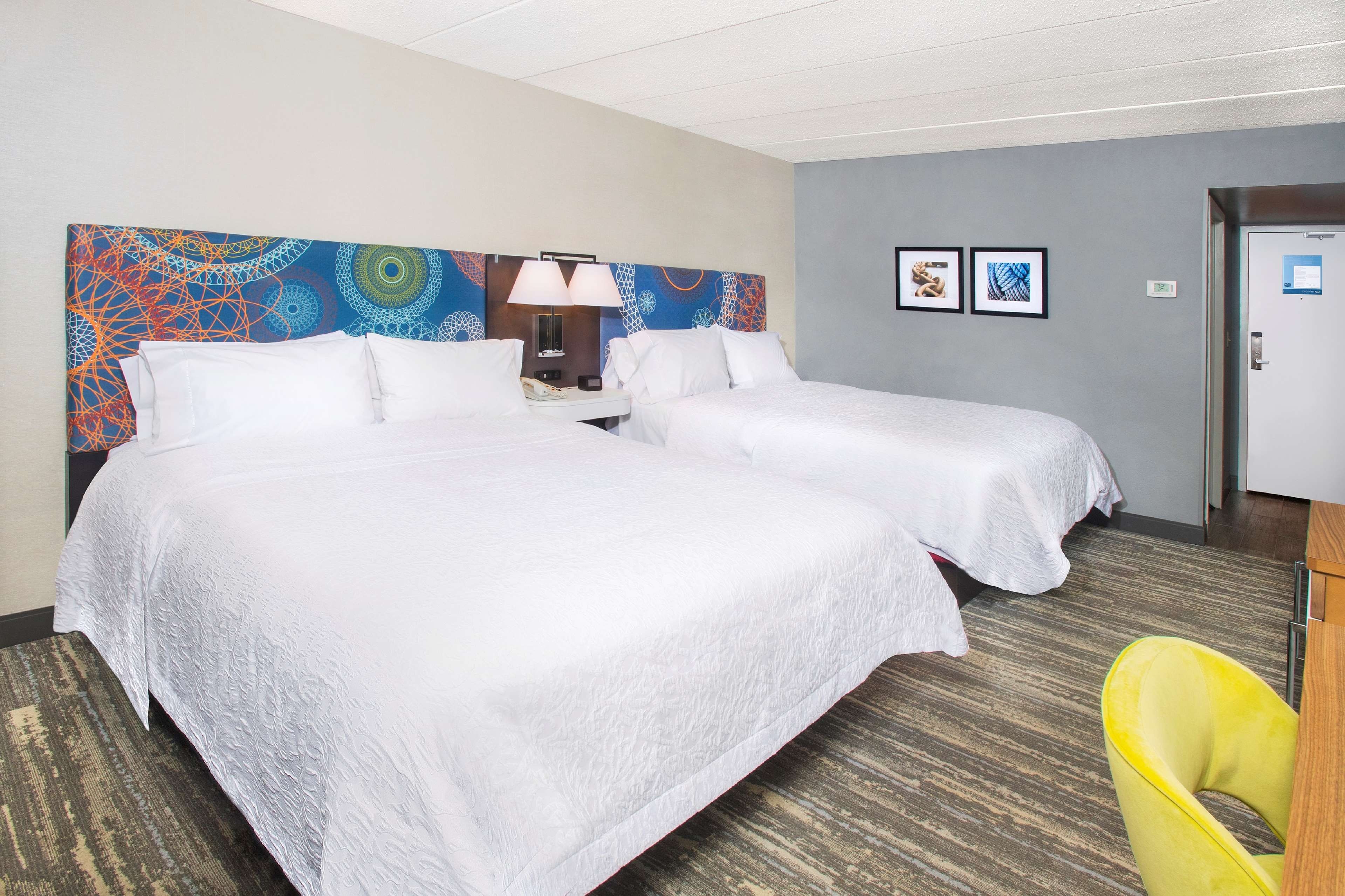 Habitación de hotel con dos camas, una mesita de noche, una lámpara y una silla.