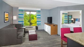 A hotel room with a sofa, a small table, a TV, a desk, a chair, and a bed.