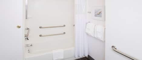 A bathroom with a bathtub, a shower, and a toilet. There are handrails and a towel rack.
