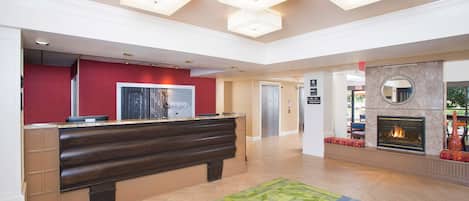 Un vestíbulo de hotel con mostrador de recepción, chimenea y alfombra colorida.