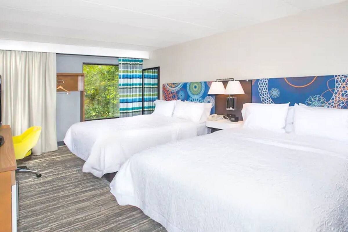 A hotel room with two beds, a desk, a chair, and a window with curtains.