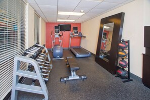 Un gimnasio con cintas de correr, elípticas, una banca y pesas sueltas.