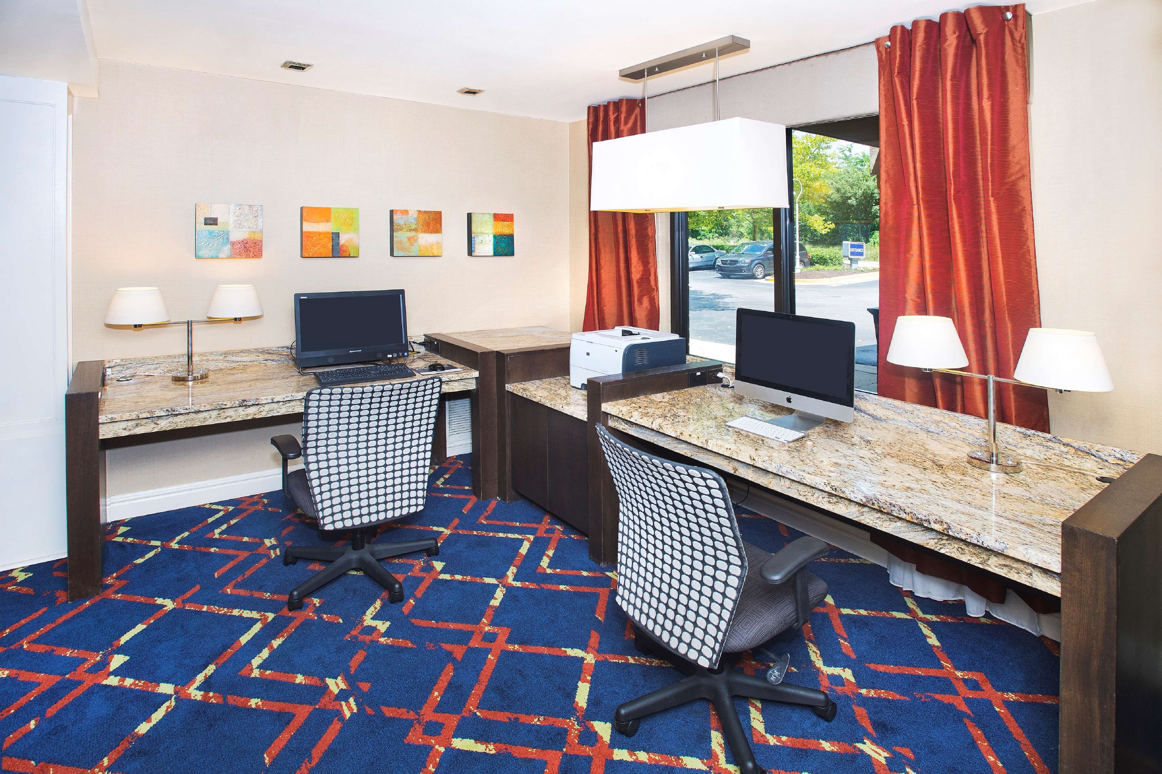 Une chambre d’hôtel avec deux bureaux, deux chaises, un sol recouvert de moquette et des œuvres d’art accrochées au mur.