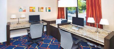 A hotel room with two desks, two chairs, a carpeted floor, and artwork on the wall.